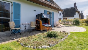 Une maison traditionnelle avec un toit de chaume, un patio avec des meubles d’extérieur et un jardin.