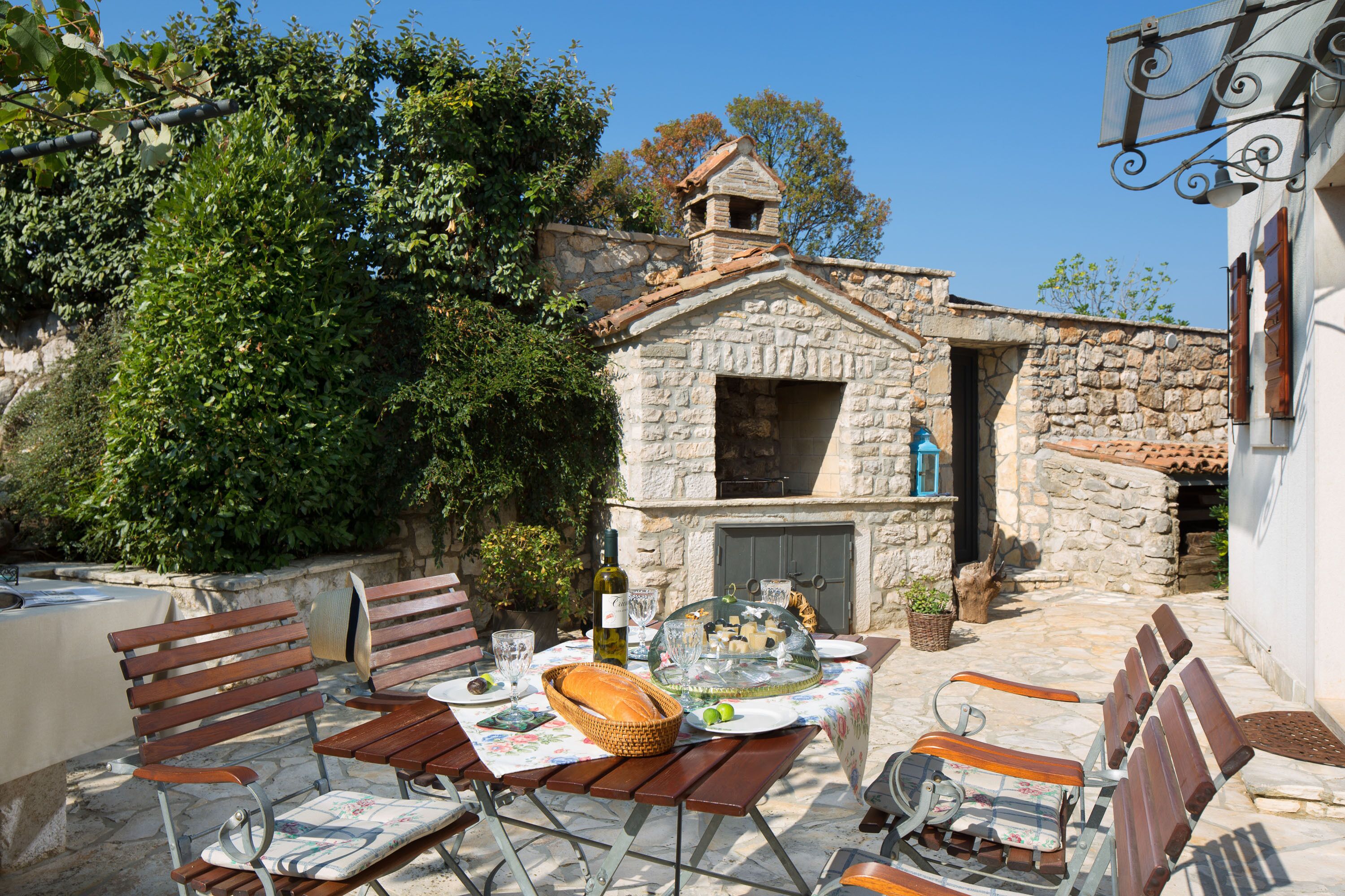 An outdoor dining area with stone walls, wooden benches, and a table set for a meal.
