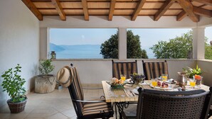 A terrace with a table set for breakfast, chairs, and a view of the sea. - Villa Primela with breathtaking sea views and private pool (Labin)