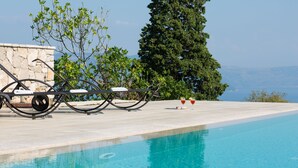 A poolside area with lounge chairs, a stone wall, and a view of the sea. - Villa Primela with breathtaking sea views and private pool (Labin)