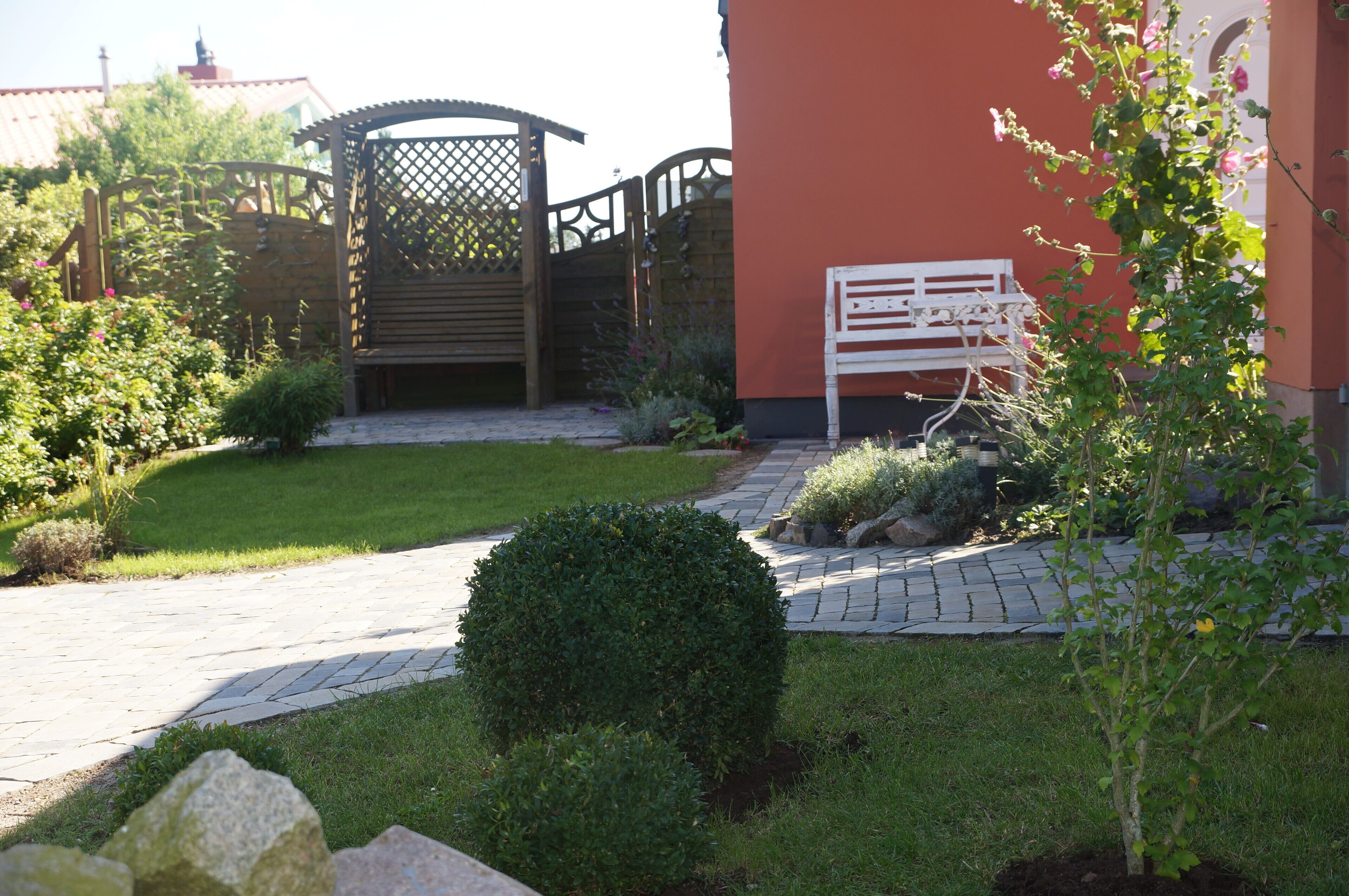 A garden with a paved pathway, a wooden gate, and a bench.