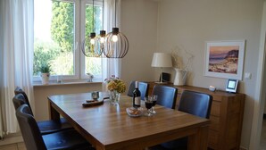 Uma sala de jantar com uma mesa de madeira, cadeiras, um candelabro, um vaso com flores, uma garrafa de vinho e um quadro emoldurado na parede.