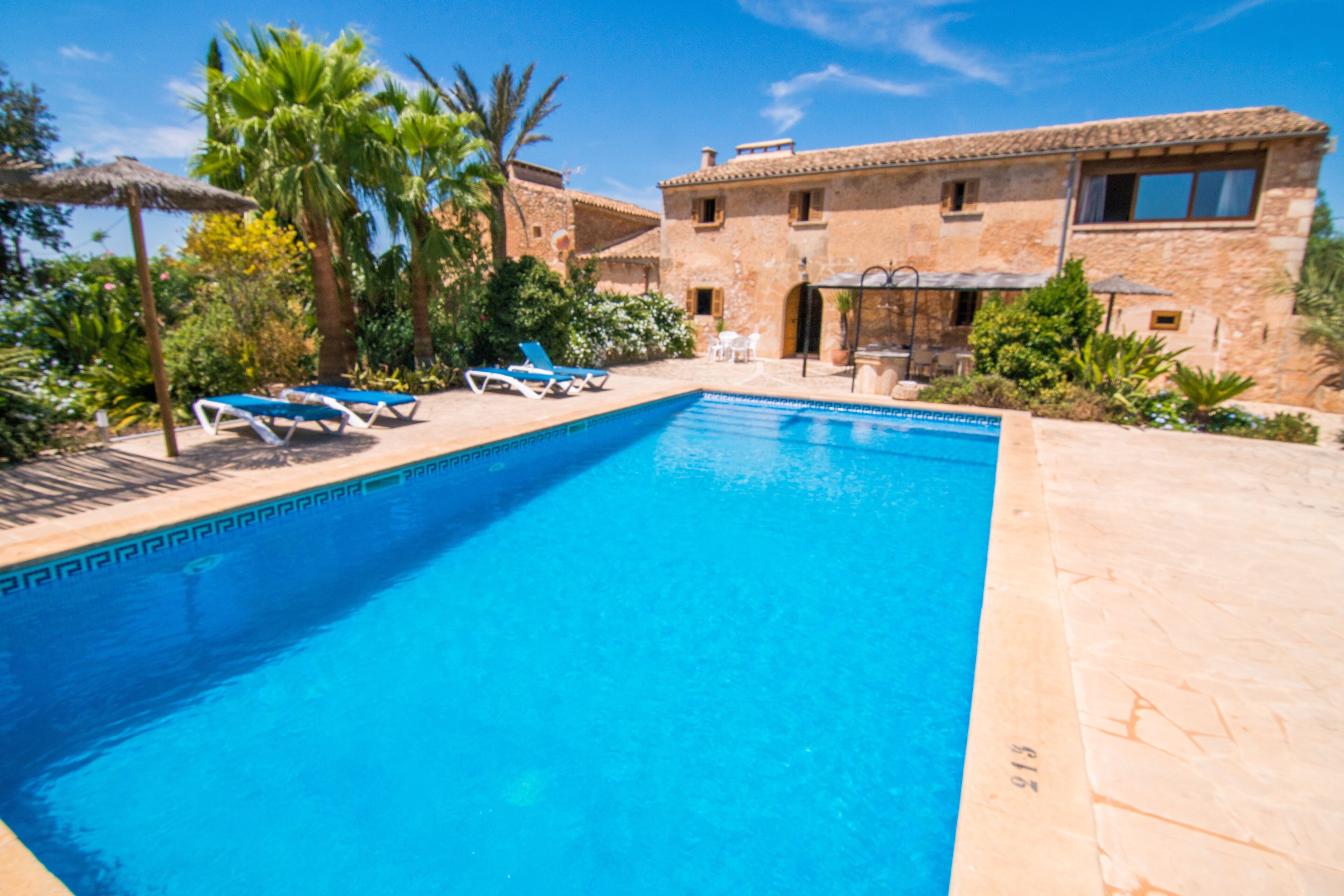 A swimming pool with lounge chairs, a stone building, and palm trees.