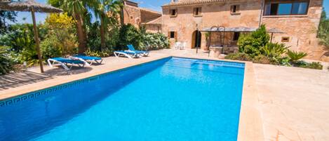 A swimming pool with lounge chairs, a stone building, and palm trees.