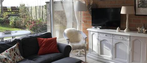 A living room with a black sofa, a white table, a patterned rug, a white armchair, a fireplace, and a TV.