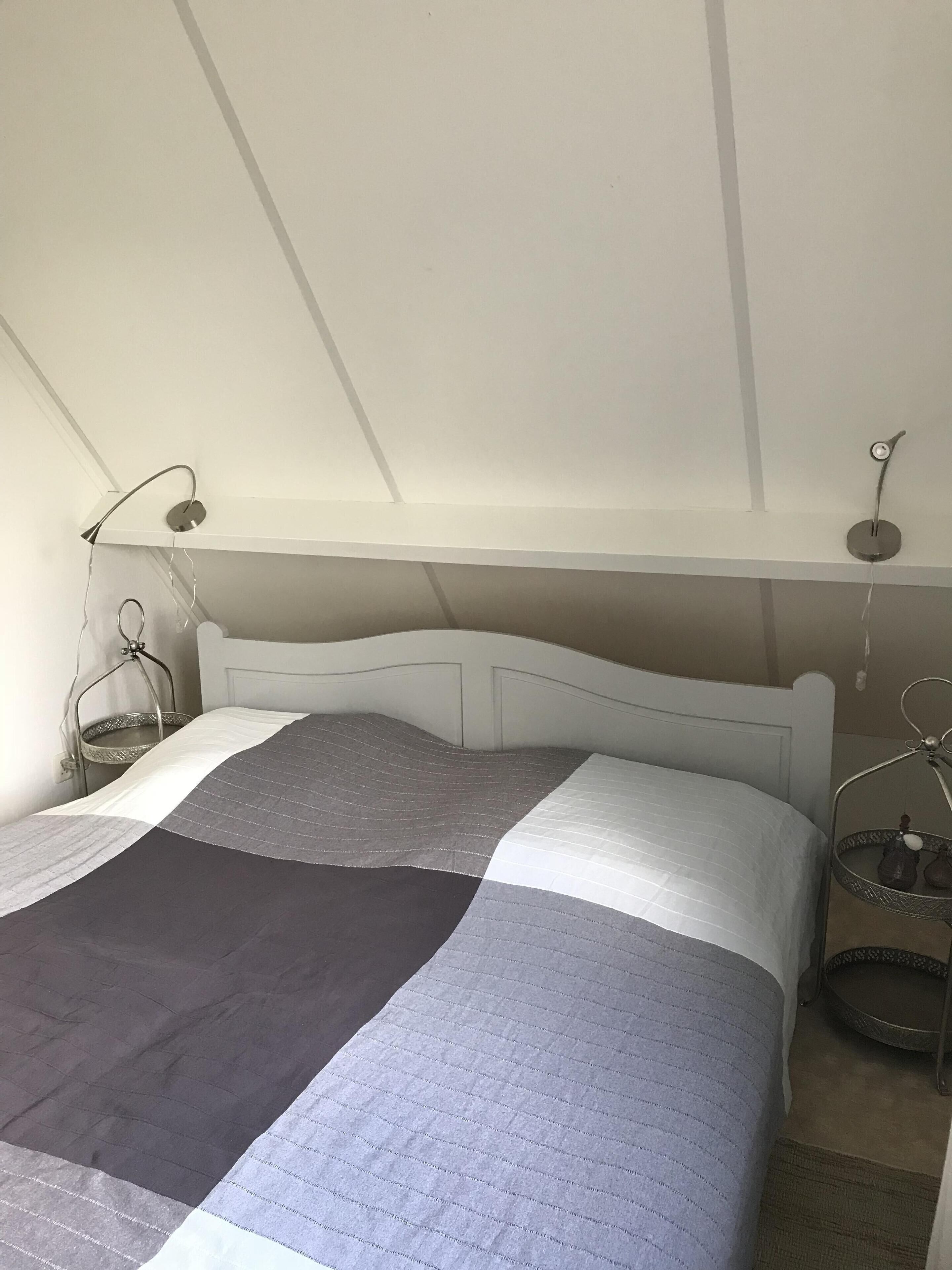 A bedroom with a bed, a bedside table, a lamp, and a hanging light fixture.