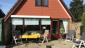 A patio with a yellow table, white chairs, and potted plants. - Detached holiday home in picturesque Noordholland, close to the beach (Sint Maartensvlotbrug)