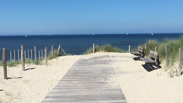 A wooden boardwalk leading to a sandy beach with a bench and a fence. - Detached holiday home in picturesque Noordholland, close to the beach (Sint Maartensvlotbrug)