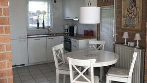 A modern kitchen with white cabinets, a dining table with chairs, a coffee machine, and a hanging light fixture. - Detached holiday home in picturesque Noordholland, close to the beach (Sint Maartensvlotbrug)
