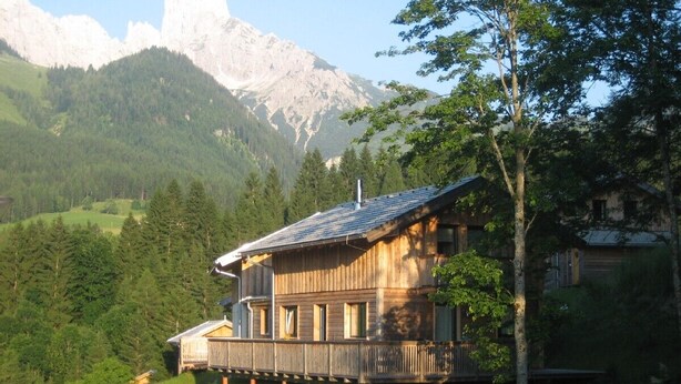 Un chalet en bois doté d’un balcon, situé dans un cadre magnifique, avec des montagnes et des arbres en arrière-plan.