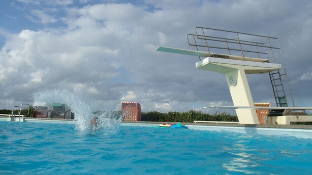 Une plateforme de plongeon avec une échelle, une piscine et, au fond, un poste de surveillance pour les sauveteurs.
