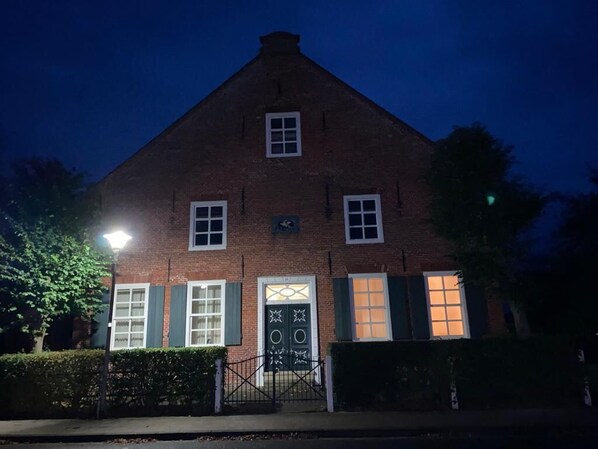 A brick building with a triangular roof, a central entrance with a decorative door, and a small sign above the door.