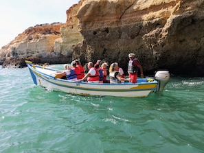 A boat with passengers wearing life jackets, a Honda outboard motor, and rocky cliffs in the background.