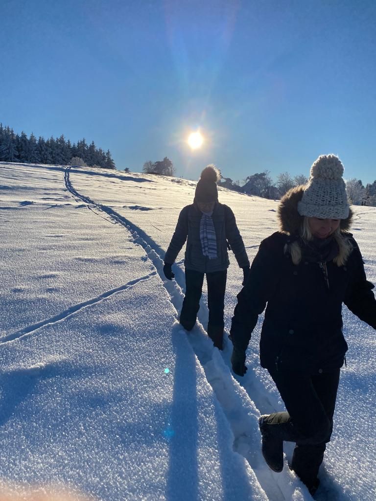 Two people walking on a snowy path with a clear sky and sun in the background.