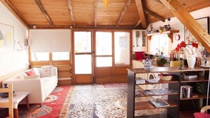 Ein gemütlicher Raum mit Holzbalkendecke, einer Stern-Dekoration, einem weißen Sofa, einem roten Teppich und einem Bücherregal.