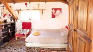 Ein gemütliches Zimmer mit einem Bett, einem roten Sessel, einem Regal mit Dekoration und einem Fenster mit Vorhängen.