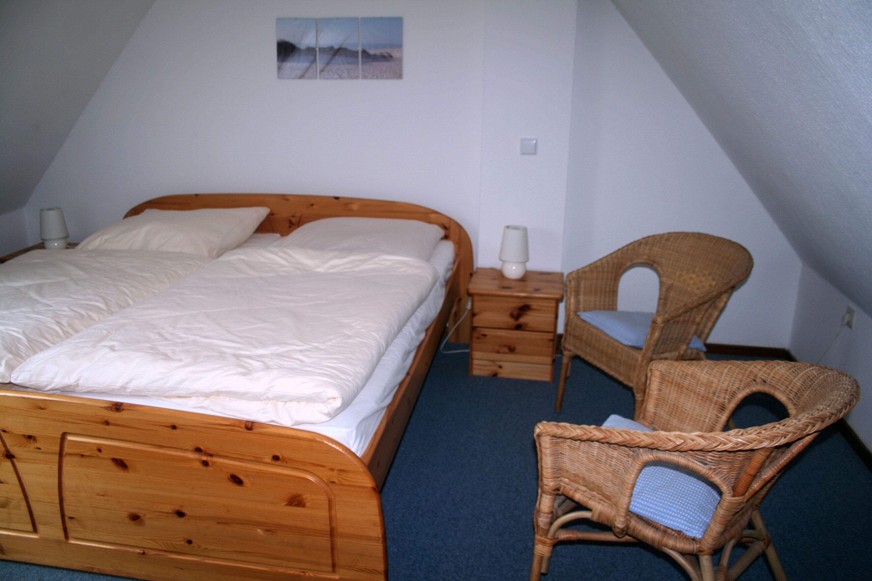 A bedroom with a wooden bed, a wicker chair, and a small bedside table with a lamp.