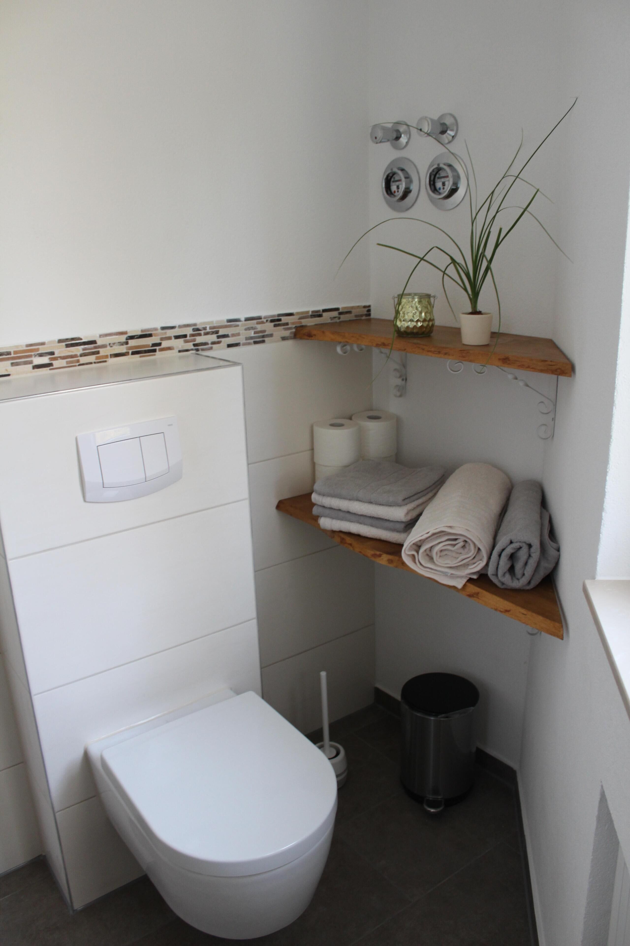 A compact bathroom with a toilet, a trash bin, and a shelf with towels and toiletries.