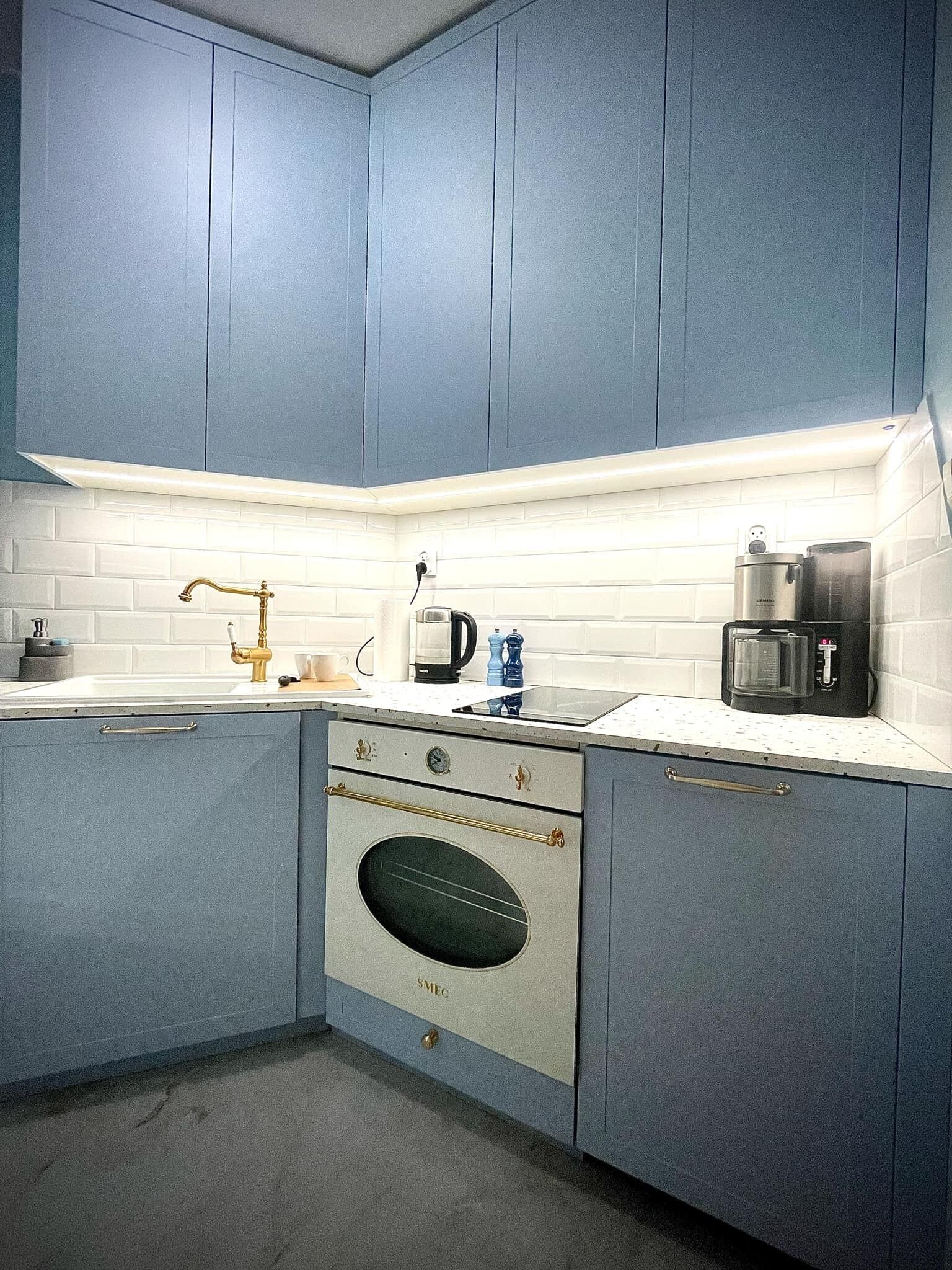 Eine Küche mit blauen Schränken, einer weißen Arbeitsplatte, einer Edelstahl-Kaffeemaschine und einem eingebauten Backofen.
