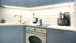Cocina con gabinetes azules, una encimera blanca, una cafetera de acero inoxidable y un horno empotrado.