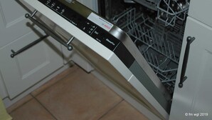 Eine Bosch Spülmaschine in einer Küche mit weißen Schränken und Fliesenboden.