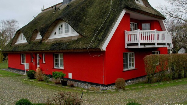 Ein rotes Haus mit einem Strohdach und einem weißen Balkon.