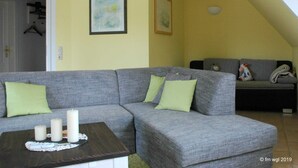 Ein Wohnzimmer mit einem grauen Ecksofa, einem kleinen Couchtisch mit Kerzen und einem grauen Sofa im Hintergrund.