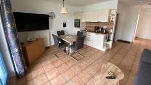 A compact living space with a dining area, kitchenette, and a TV mounted on the wall. - Pure nature - attractive apartment on Cape Arkona, the northernmost point of Rügen (Putgarten)