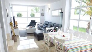 Ein helles Wohnzimmer mit einer Couch, einem Couchtisch und einem Essbereich mit gestreiftem Tischläufer.