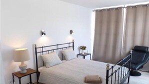 Ein Schlafzimmer mit einem Bett, Nachttischen, einer Lampe, einem Stuhl und einem Fenster mit Vorhängen.