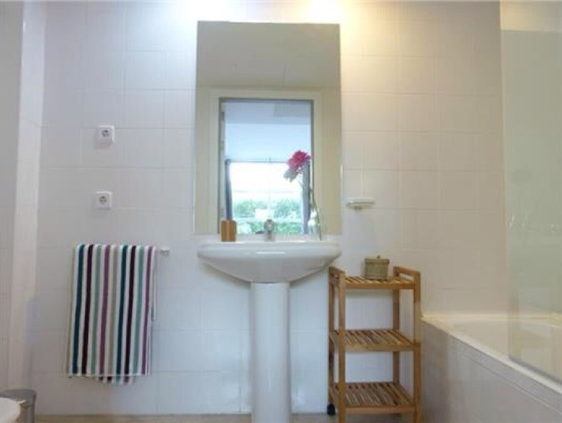 A bathroom with a white sink, a window, a striped towel, and a wooden shelf.