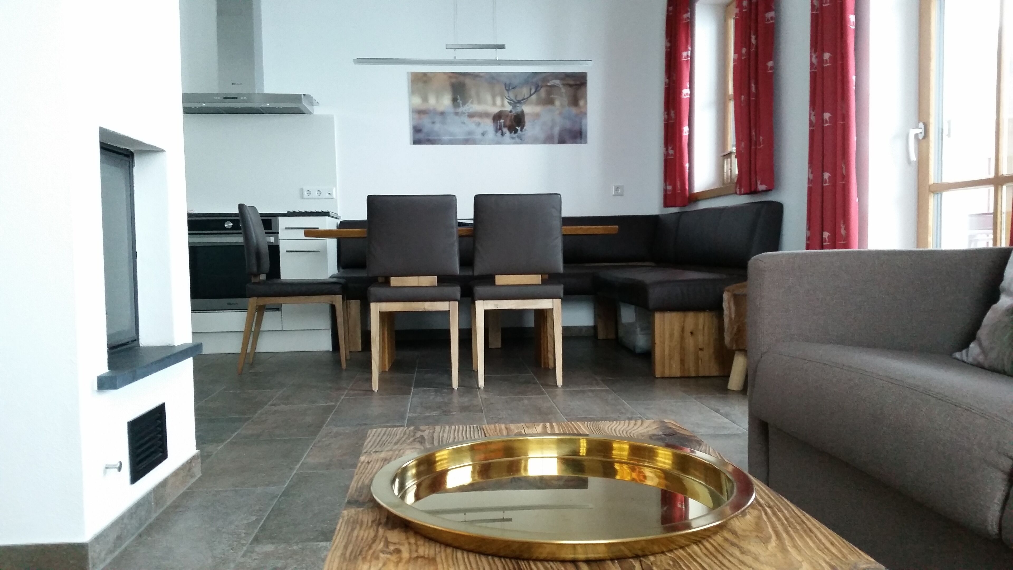 Uma sala de estar moderna com um sofá cinzento, uma área de jantar com mesa e cadeiras, e uma cozinha ao fundo.