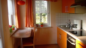 Eine kleine Küche mit Essbereich, einem Fenster mit Vorhängen und einem Spülbecken.