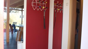 Ein Flur mit roten Wänden, Fliesenboden und Holzboden. Zwei Wanddekorationen und eine Tür zu einem anderen Raum sind zu sehen.