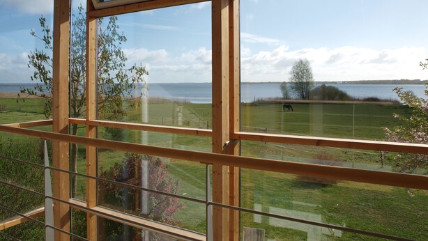 Ein Zimmer mit großen Fenstern und Blick auf eine Wiese und ein Gewässer.