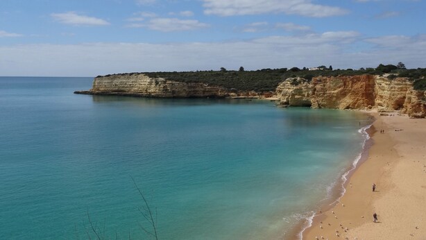 A coastal beach with clear turquoise waters, sandy shore, and rocky cliffs.