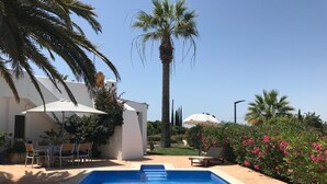 A swimming pool with a clear blue water, surrounded by palm trees and a white building with outdoor seating.