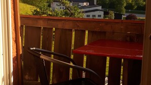 A wooden deck with a red table and metal chairs, overlooking a mountainous landscape with houses and greenery. - 80 sqm apartment, 2 bedrooms to 5 pers., 2 balconies, sunny & quiet (Berchtesgaden)