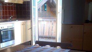 A kitchen with wooden cabinets, a checkered tablecloth, a refrigerator, and a view of a wooden deck. - 80 sqm apartment, 2 bedrooms to 5 pers., 2 balconies, sunny & quiet (Berchtesgaden)