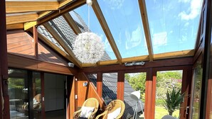 Eine sonnendurchflutete Terrasse mit Korbmöbeln, einer Glaskuppel und Blick auf den Garten.