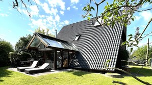 Ein modernes Haus mit Satteldach, einer überdachten Terrasse mit Liegestühlen und einem gepflegten Rasen.