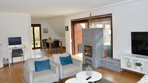 Ein modernes Wohnzimmer mit Kamin, Fernseher und einem Essbereich im Hintergrund.