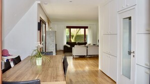 Eine moderne Küche mit weißen Schränken, einem Holztisch und Blick auf einen Wohnbereich mit Sofa und Fenster.