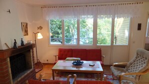 A cozy living room with a fireplace, a red sofa, a wooden coffee table, and a white armchair.