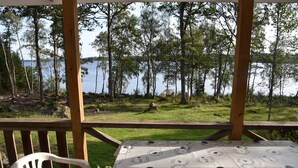 A wooden deck with a table covered in a patterned tablecloth, overlooking a lake with trees and grassy areas.