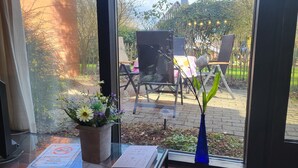 A view through a window of an outdoor seating area with chairs and tables, a potted plant, and a blue vase. - Apartment Berg & Barkenhoff vis-à-vis the Barkenhoff for 1-5 people (Worpswede)