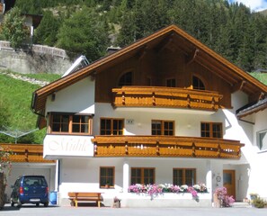 Un edificio a due piani con un balcone, un cartello con la scritta 'Mitte' e un'auto parcheggiata di fronte.