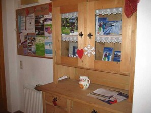 Un armadietto in legno con scomparti multipli, una bacheca con diversi documenti e una tazza a motivi floreali sul bancone.