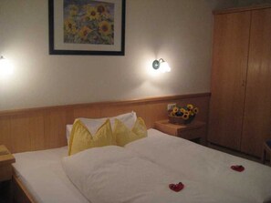 Una camera d'albergo con un letto, un comodino, una lampada a parete, un quadro di girasoli e un armadio in legno.