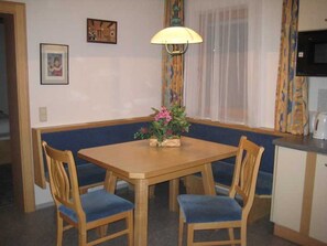 Un'angolatura sala da pranzo con tavolo di legno, due sedie, una panca, una lampada e una finestra con tende.